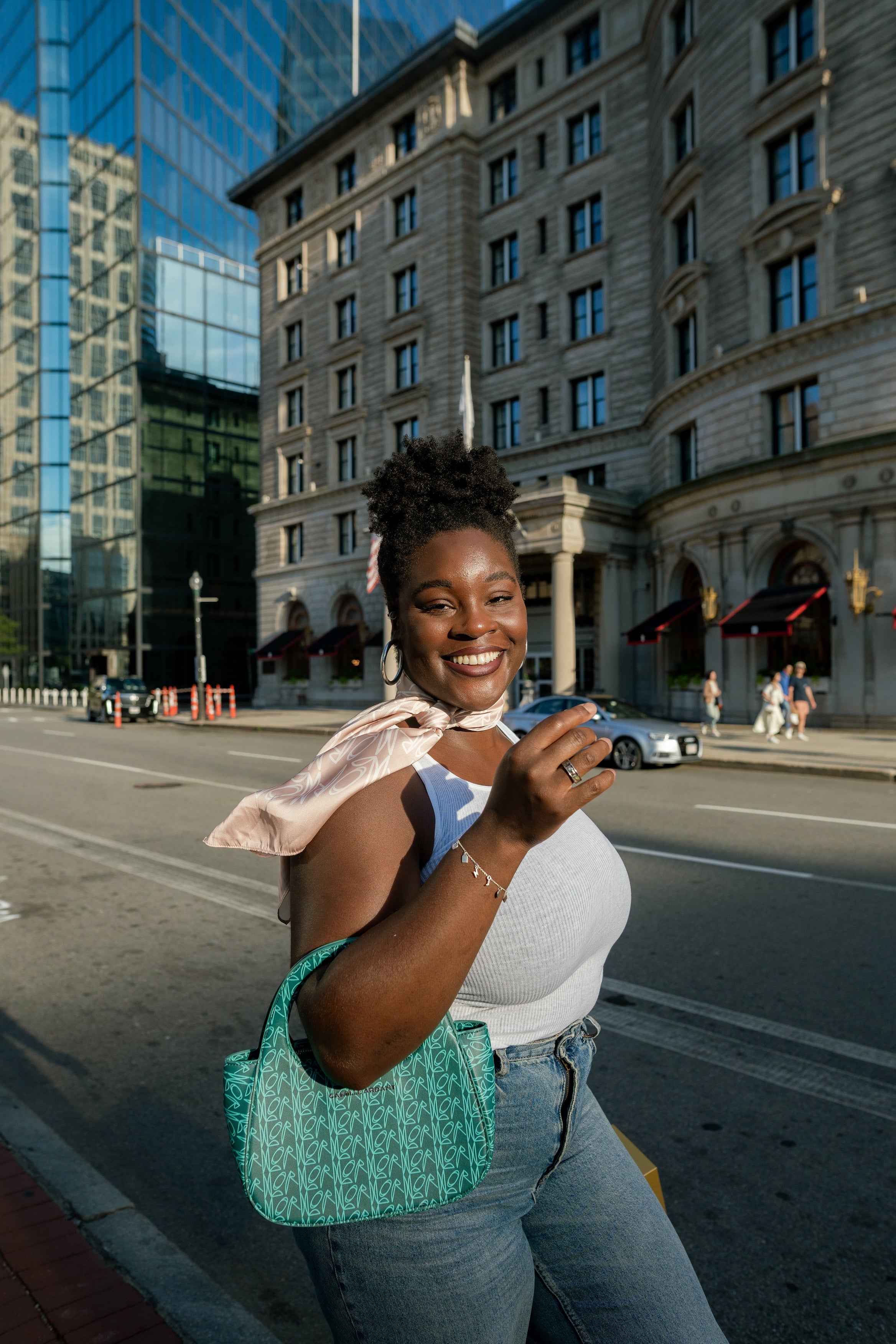 Woman standing on a city street holding Lagoon Teal Genesis Bag with modern and classical architecture in the background